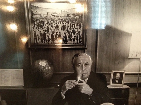 Harold Wilson lights his pipe in front of a painting by LS Lowry