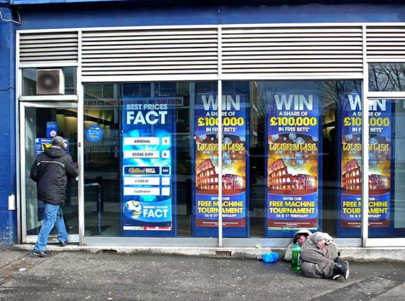 A man walking into a bookmakers while a homeless man lies on the ground outside