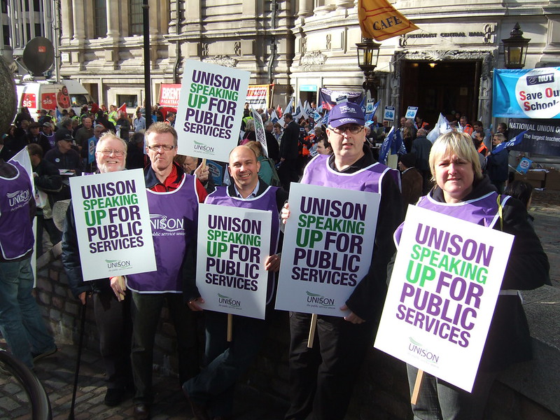 A group of people in UNISON bibs with placards that say "UNISON SPEAKING UP FOR PUBLIC SERVICES"