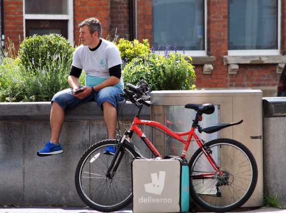 A Deliveroo rider waits by his bike with a Deliveroo bag by its side
