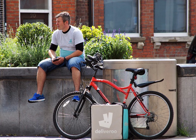 A Deliveroo rider waits by his bike with a Deliveroo bag by its side